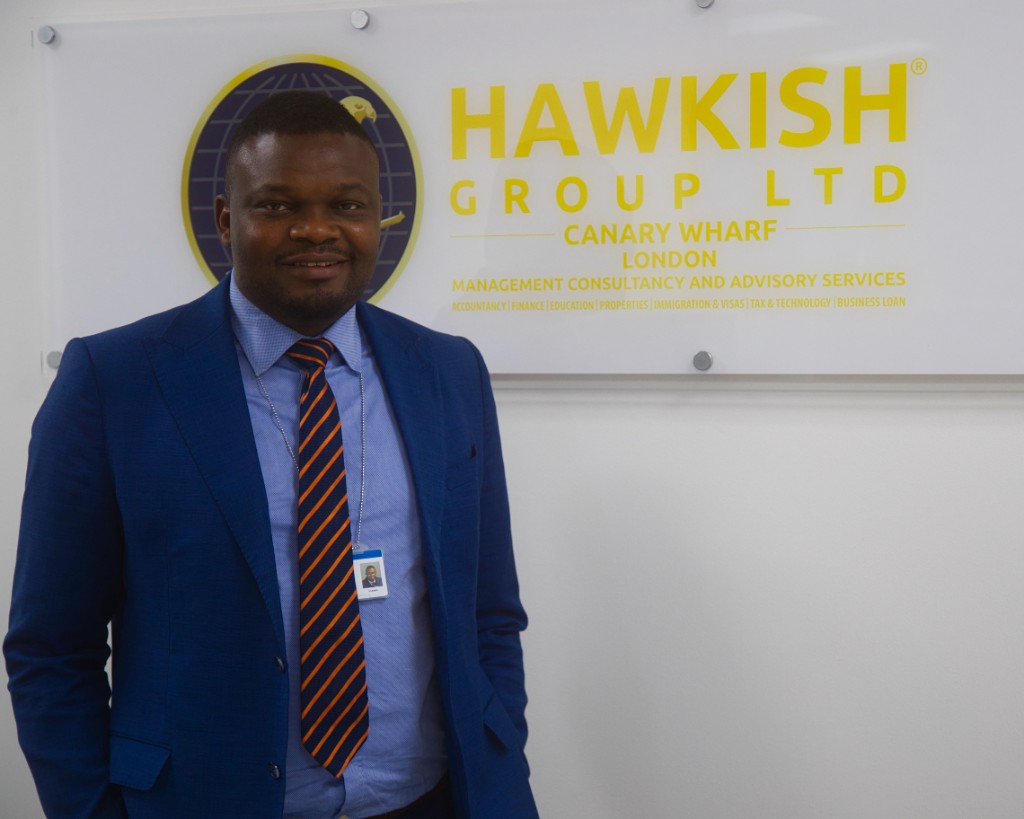 Usman Ayankoya, Founder of Hawkish Group, standing in front of the Hawkish Group Ltd sign at Canary Wharf, London